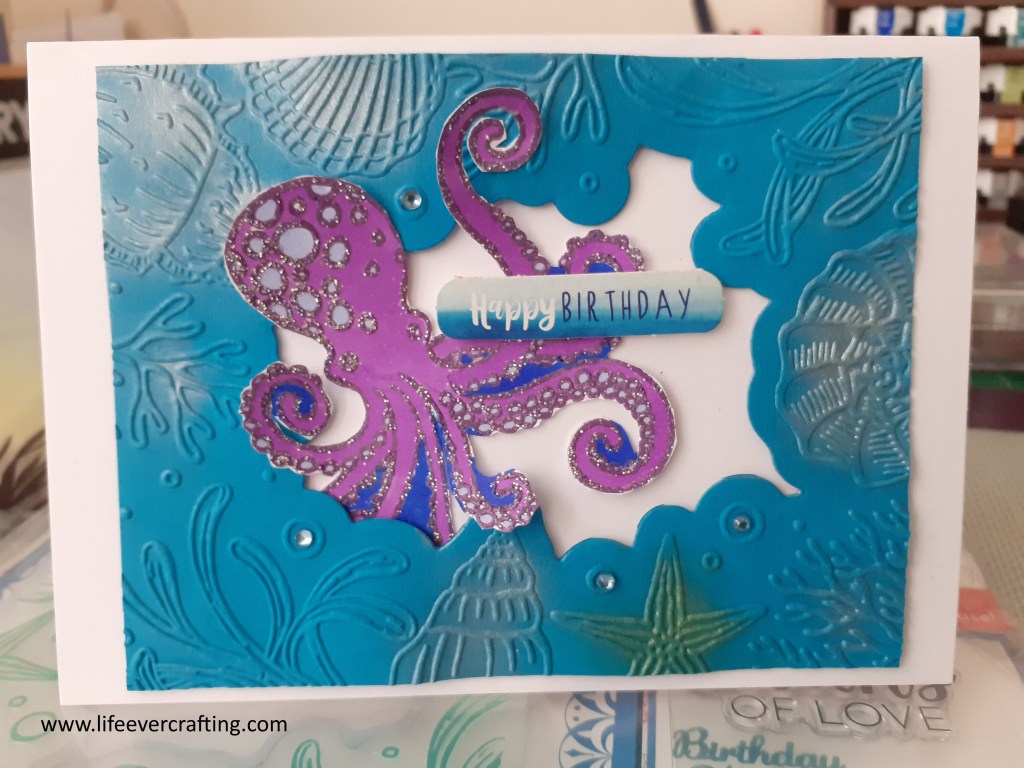 Image shows a purple octopus surrounded by a blue frame of shells and seaweed. There is a blue sentiment reading Happy Birthday in the centre of the card.