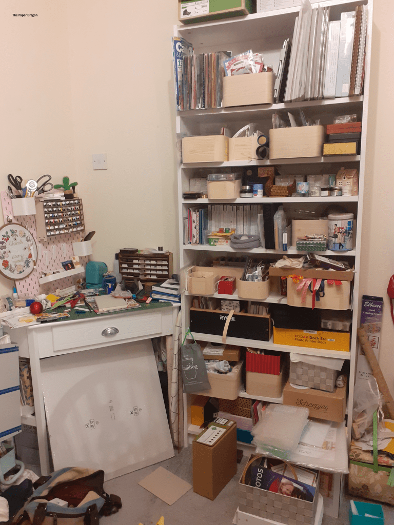 Image shows a desk and bookcase overflowing with craft supplies.