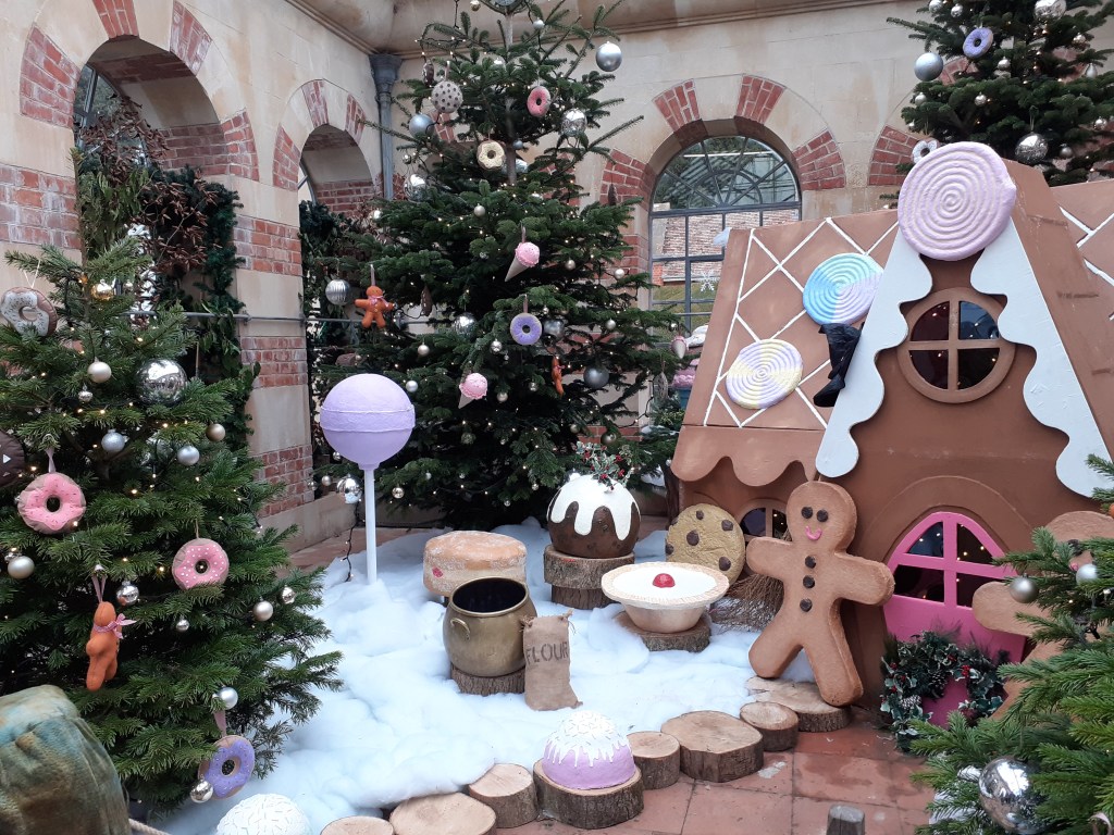 image shows a gingerbread house surrounded by Christmas trees decorated with sweet treats.