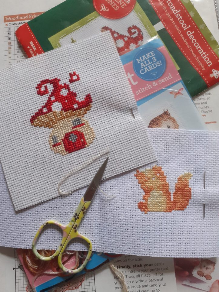 image shows two cross stitch pictures, one of a toadstool house and the other of a fox